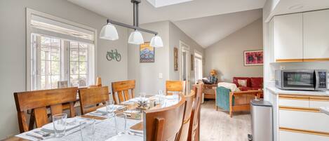 A dining area with a wooden table set for four, a kitchen with white cabinets, and a red sofa in the background.