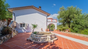 A white building with a tiled patio, stone walls, and a fountain.