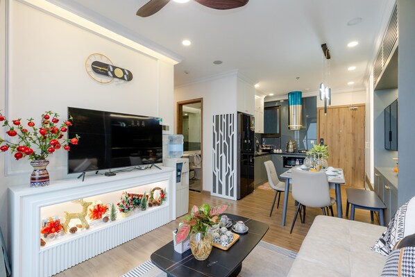 A modern living room with a flat-screen TV, a fireplace, and a dining area with a table and chairs. - Friendly House QMP - Ecopark (Van Giang)