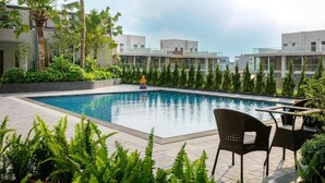 A swimming pool with surrounding greenery and modern buildings in the background. - Friendly House QMP - Ecopark (Phung Cong)