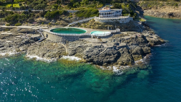 Um imóvel costeiro com piscina, um edifício com varanda e vista para o mar e colinas.
