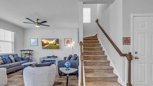 A living room with a staircase, a ceiling fan, and a 'No Shoes Upstairs' sign. - Stylish Beach Retreat | Close to Everything| 4 Bed (Myrtle Beach)