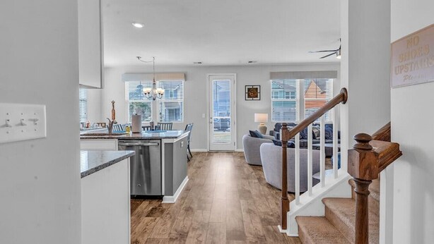 A modern kitchen with a central island, a dining area with a sofa, and a staircase with a wooden handrail. - Stylish Beach Retreat | Close to Everything| 4 Bed (Myrtle Beach)