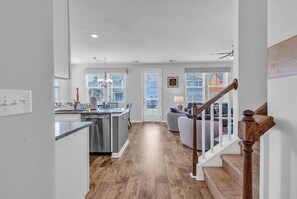 A modern kitchen with a central island, a dining area with a sofa, and a staircase with a wooden handrail. - Stylish Beach Retreat | Close to Everything| 4 Bed (Myrtle Beach)