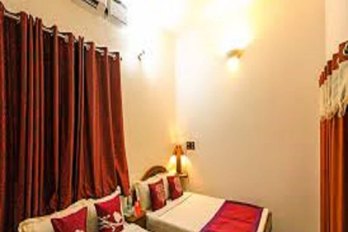 A hotel room with two beds, red curtains, a wall-mounted air conditioner, and a bedside lamp.