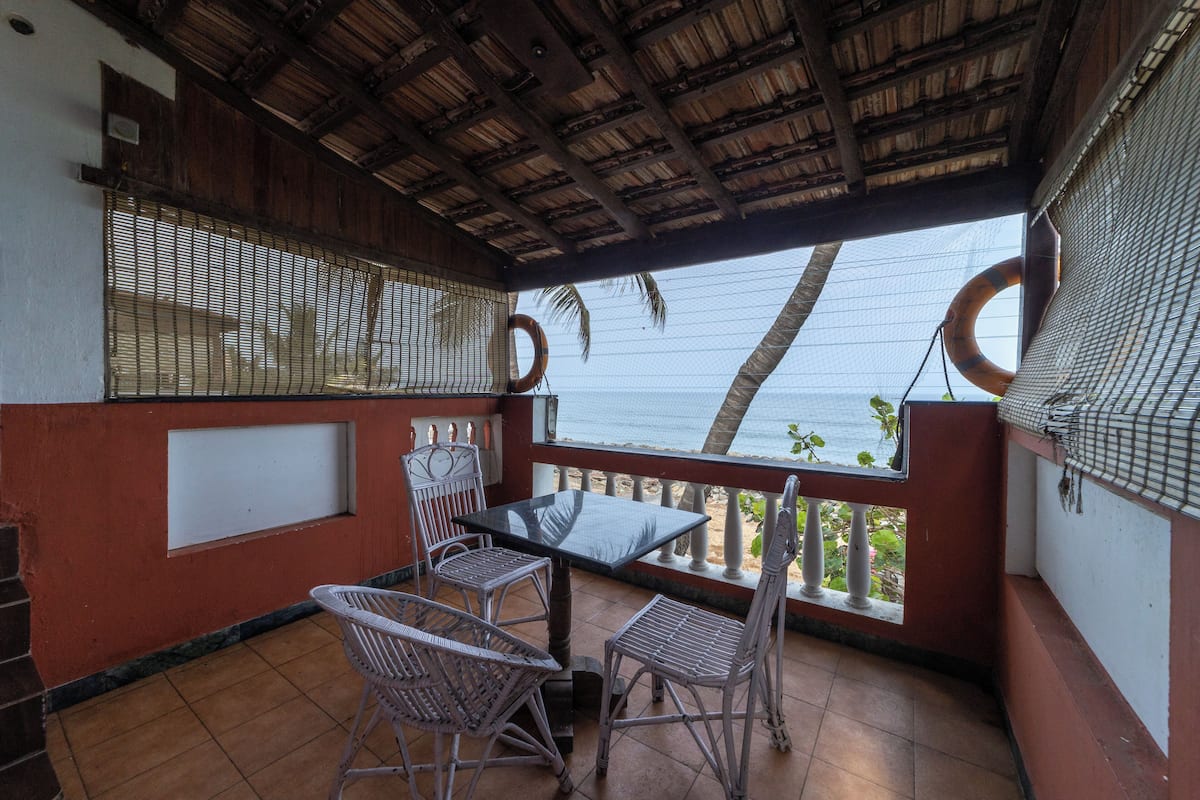 A covered outdoor area with a table and chairs, a view of the ocean, and a thatched roof.