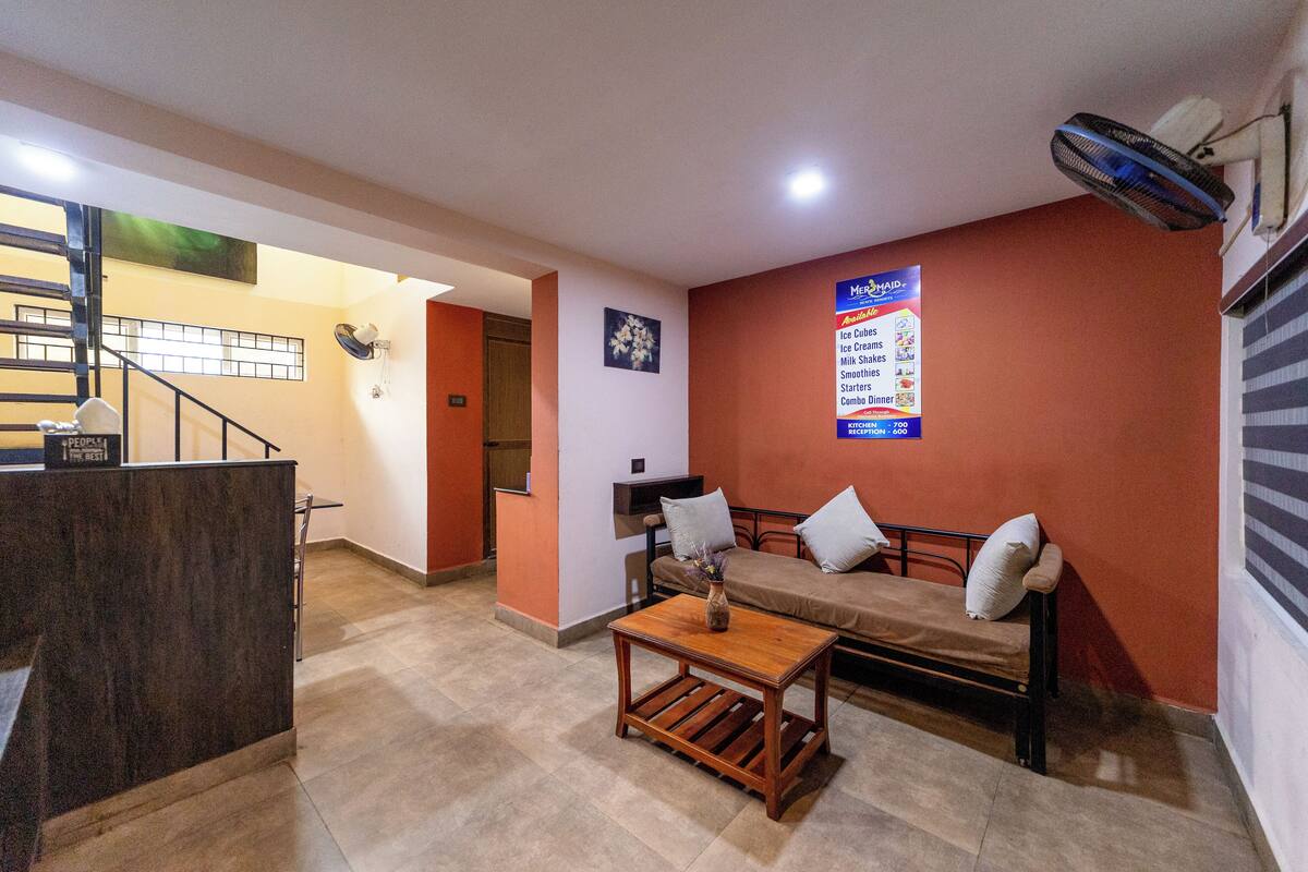 A hotel lobby with a reception desk, a sofa with pillows, a wooden table, and a wall sign listing amenities.