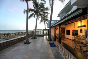 Um restaurante à beira-mar com mesas ao ar livre, palmeiras e vista para o oceano.