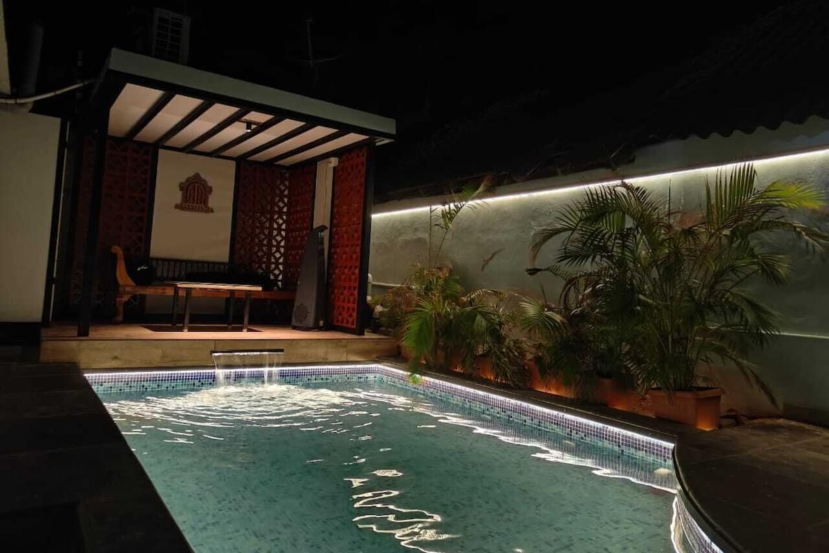 A swimming pool with a tiled edge and a bench. There are potted plants around the pool.