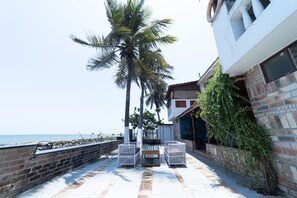 A patio with two white wicker chairs and a small table, a palm tree, and a view of the sea. - Mermaid  Island Beach Resort (Vanur)