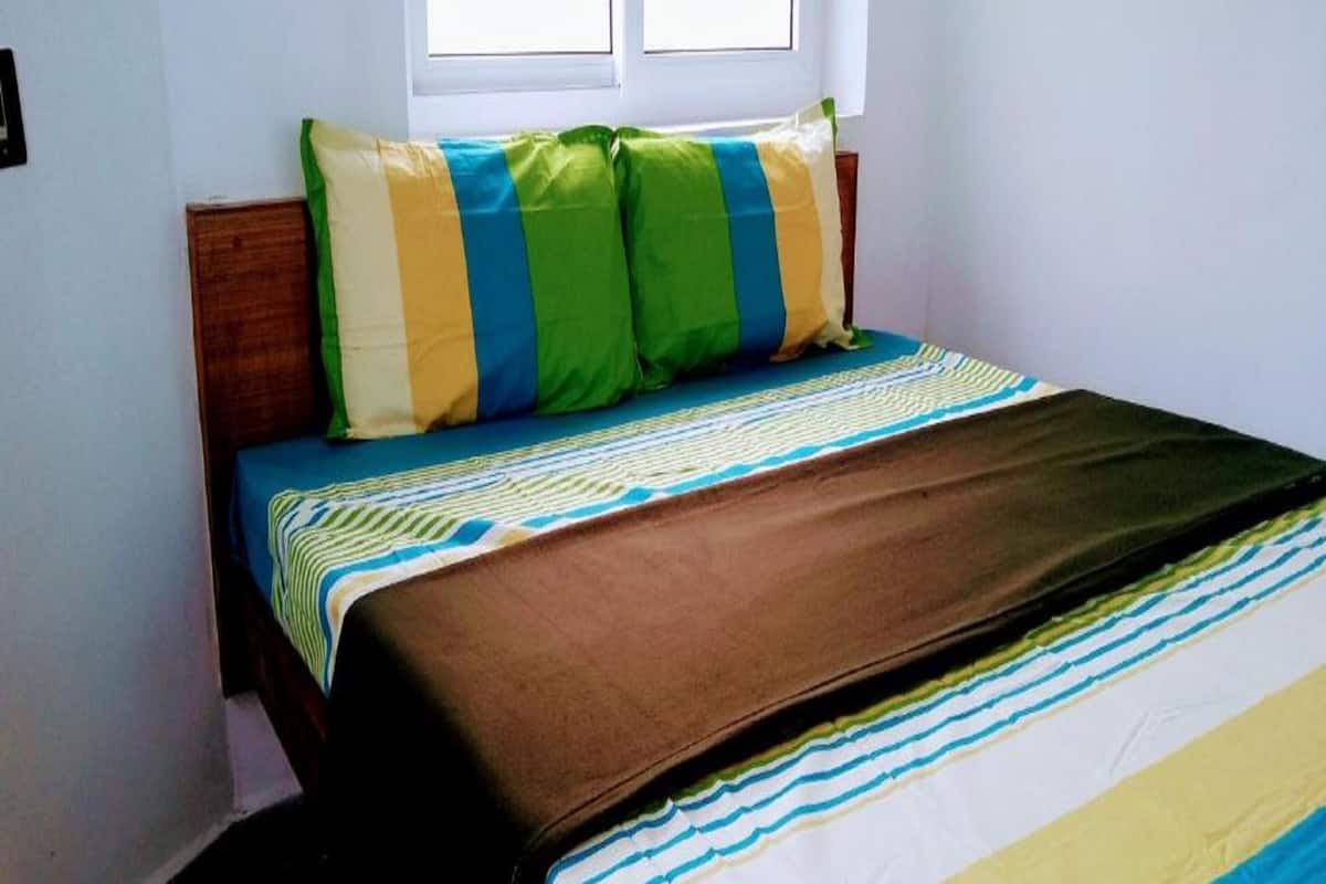 A bed with striped bedding, a window with blinds, and a wooden headboard.