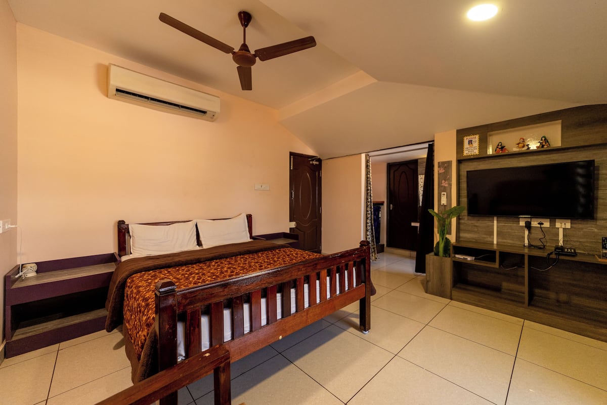 A bedroom with a bed, a ceiling fan, an air conditioning unit, a TV, and a wooden TV stand.