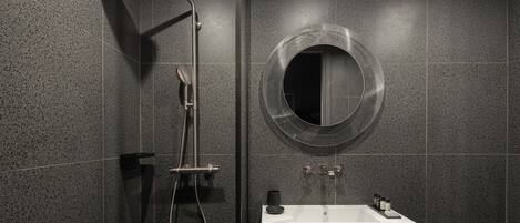 A modern bathroom with a freestanding shower, a round mirror, and a white sink.