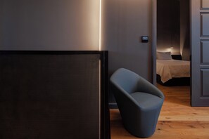 Een moderne kamer met een donkergrijze bank, een bed met een witte dekbedovertrek en een bedieningspaneel aan de muur.