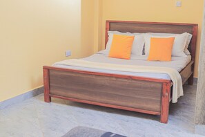 Un letto con struttura in legno e biancheria bianca, una parete gialla e un pavimento piastrellato.