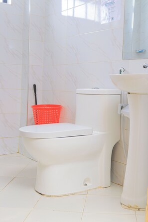 A bathroom with a toilet, a sink, and a red basket.