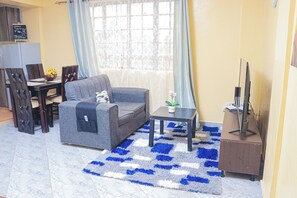 A living room with a sofa, a coffee table, a TV stand, and a dining area with chairs and a table.