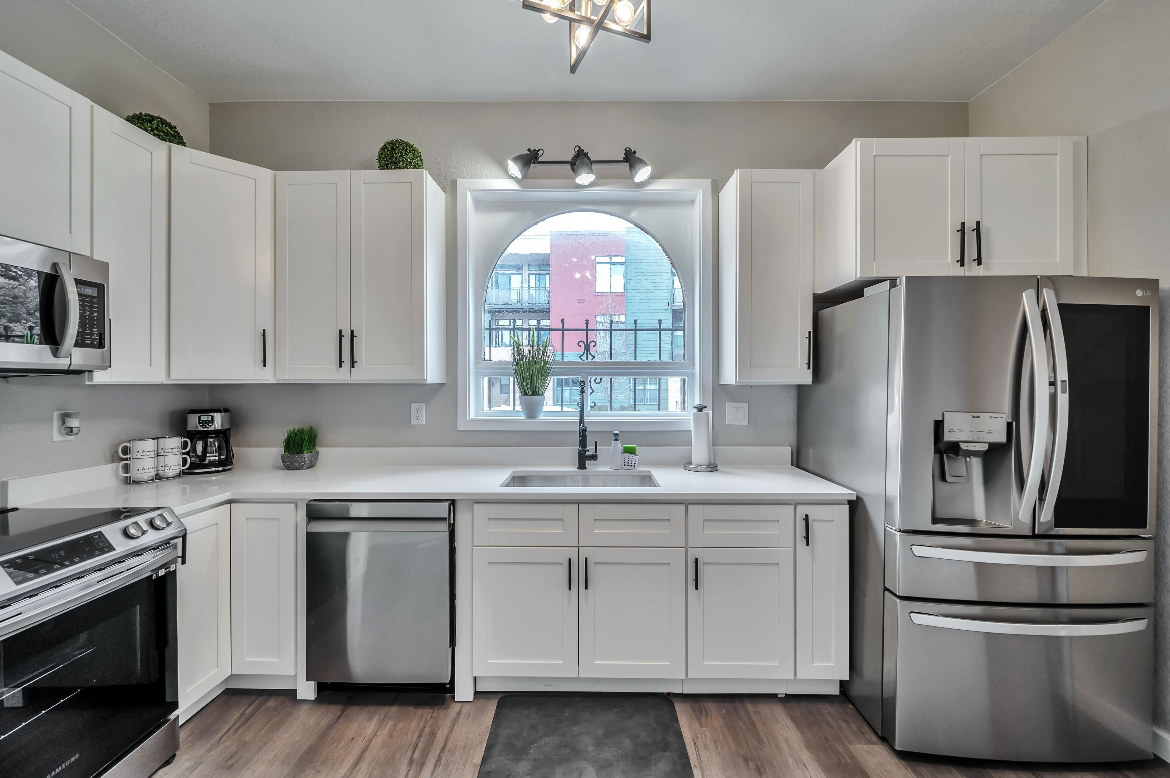 A modern kitchen with white cabinets, stainless steel appliances, a built-in oven, and a window with a view of buildings.