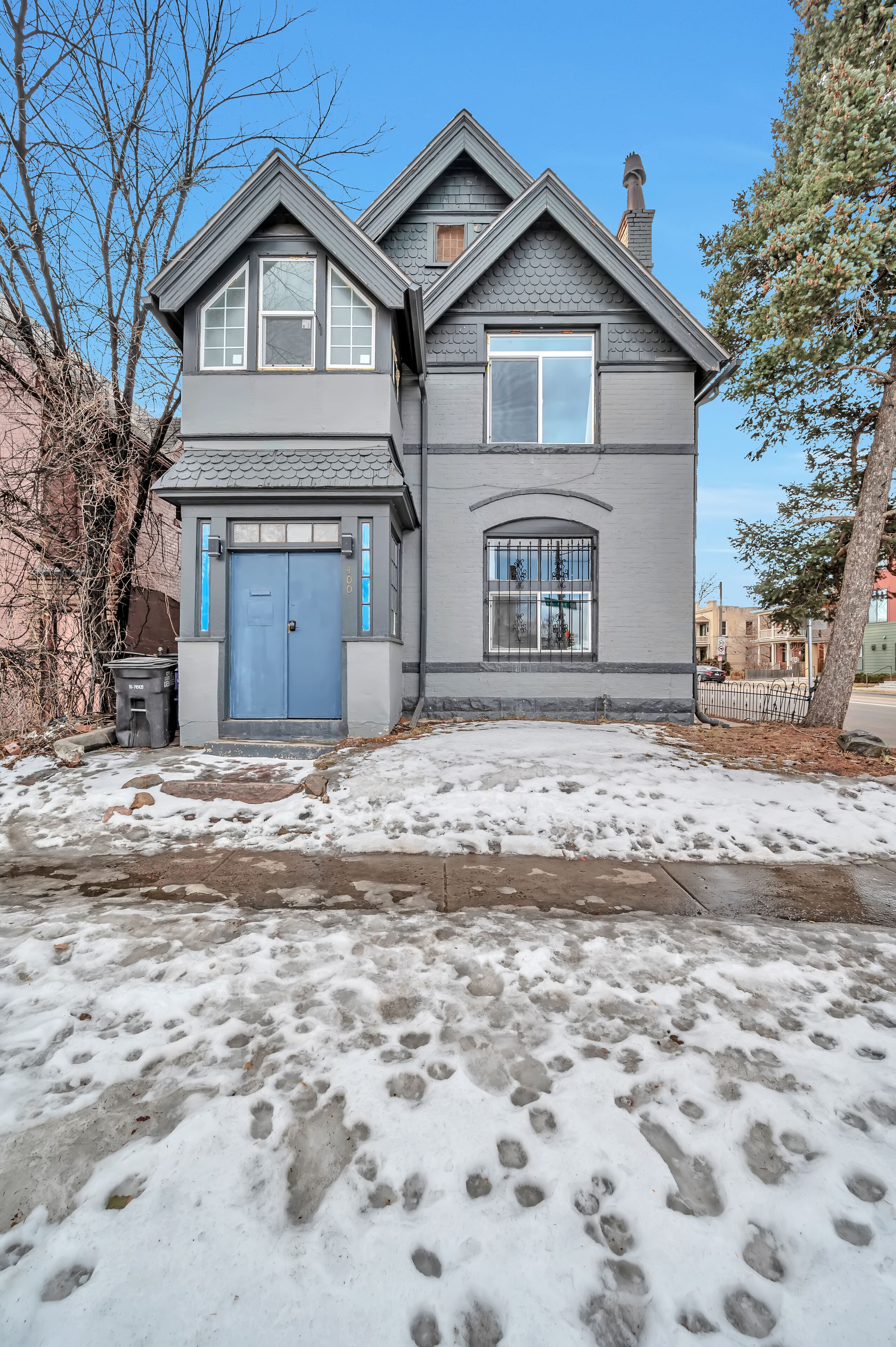 A two-story house with a blue front door, a garage, and a visible driveway with snow and footprints.
