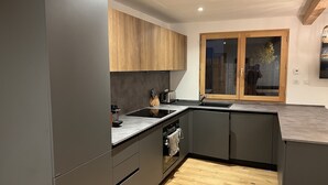 A modern kitchen with dark cabinets, a wooden countertop, and a built-in oven. - Superbe Appartement Chalet Pieds des Pistes et des Bains (Le Monêtier-les-Bains)