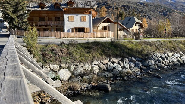 A chalet-style building with multiple balconies, a wooden deck, and a view of a river and mountains. - Superbe Appartement Chalet Pieds des Pistes et des Bains (Le Monêtier-les-Bains)