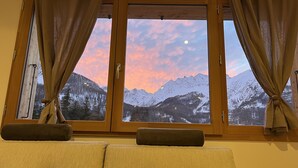 A room with a large window overlooking a snowy mountain range during sunset. - Superbe Appartement Chalet Pieds des Pistes et des Bains (Le Monêtier-les-Bains)