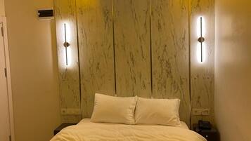 Habitación de hotel con cama, mesitas de noche y pared de madera con iluminación integrada.