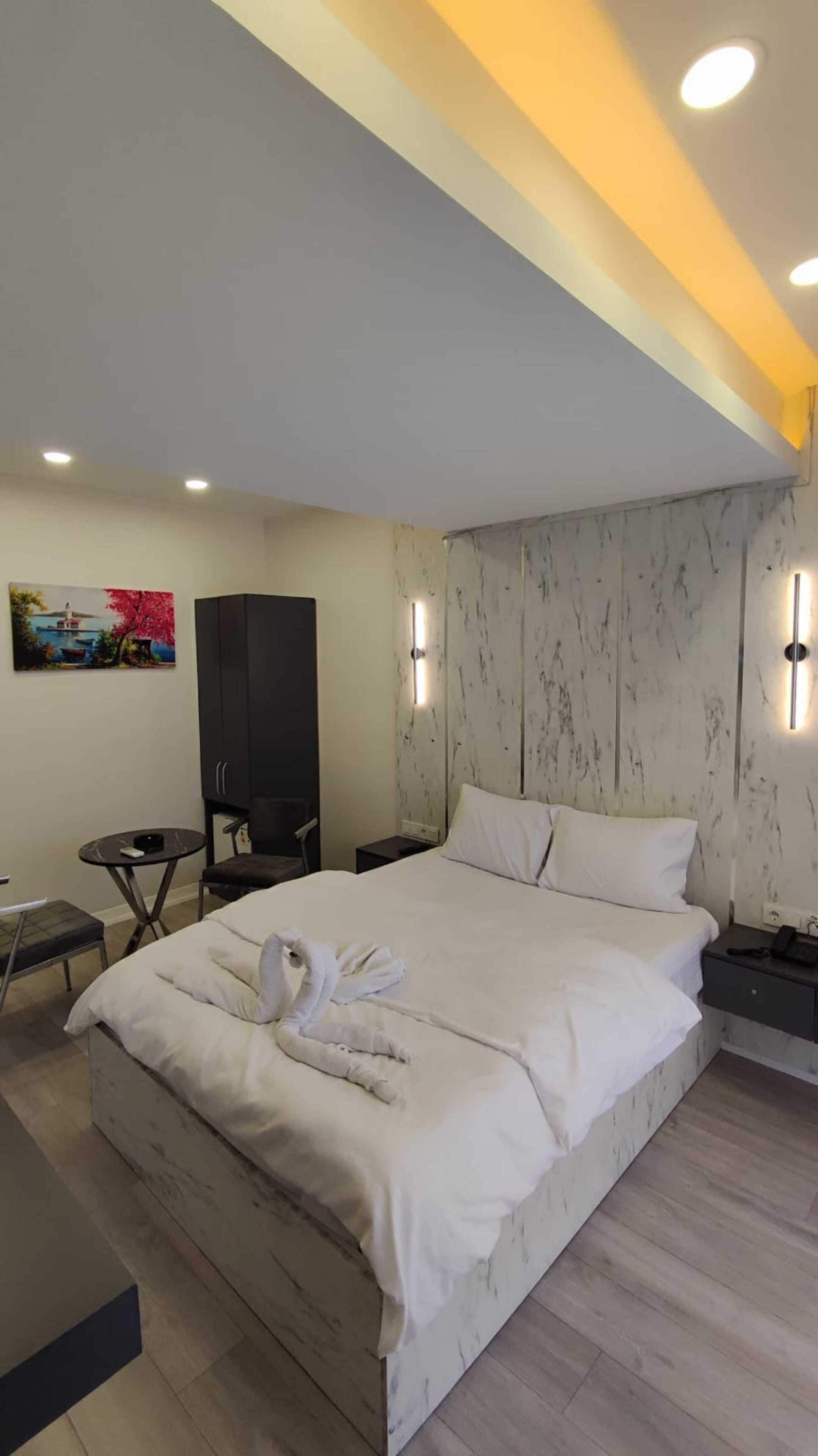 A modern hotel room with a large bed, a desk, a chair, a TV, and a painting on the wall.