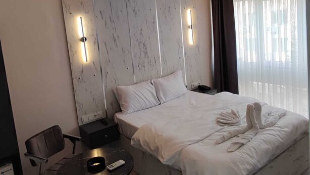 Habitació d'hotel moderna amb un llit gran, una taula rodona petita, una cadira i una tauleta de nit.