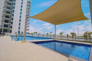 Relax by the rectangular pool surrounded by a light-colored deck and a large shade sail.