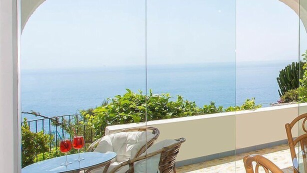 A balcony with a clear view of the sea, wicker furniture, and two red glasses on a table. - Villino Cara: A welcoming townhouse which faces the sun and the sea, with Free WI-FI. (Conca dei Marini)