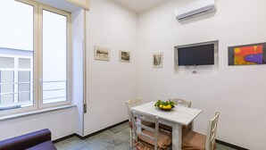 Un petit coin repas avec une table et des chaises, une fenêtre avec des stores et un téléviseur à écran plat fixé au mur.