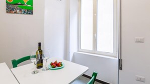 A dining area with a white table, green chairs, a bottle of wine, glasses, and a plate of strawberries. - Studios 1 in Napoli With 1 Bathrooms (Naples)