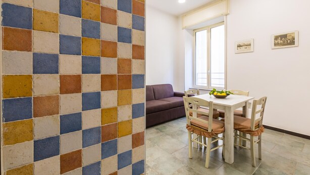 Een zithoek met een betegelde muur in ruitpatroon, een eettafel met stoelen, een bank en een raam met uitzicht.