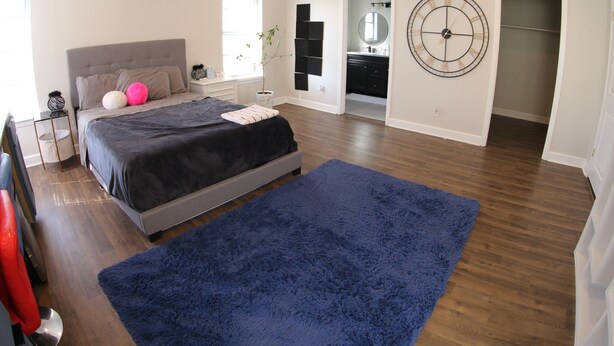 Une chambre à coucher avec un lit, un tapis bleu, un ventilateur de plafond et une horloge murale.