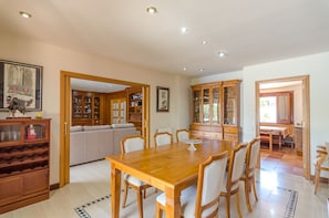 A spacious dining area with a wooden table and chairs, surrounded by wooden cabinets and a white sofa.