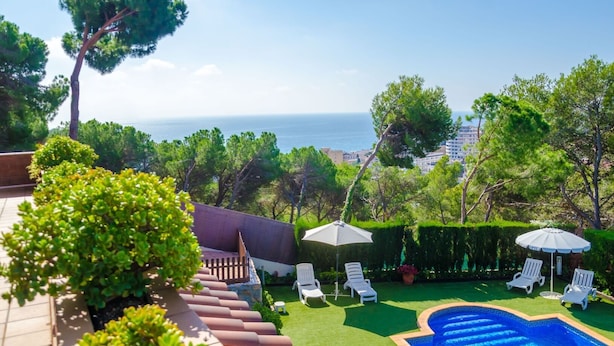 A pool area with a view of the sea, surrounded by greenery and white lounge chairs. - Club Villamar - Superbly presented family villa located in one of the most beautiful neighbourhoo... (Lloret de Mar)