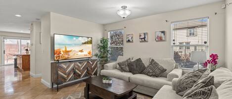 Un salon moderne avec un téléviseur à écran plat, un ensemble de canapés, une table basse et une plante décorative.