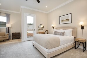 A bedroom with a large bed, a door leading to a balcony, a chair, a nightstand, and a wall-mounted lamp.