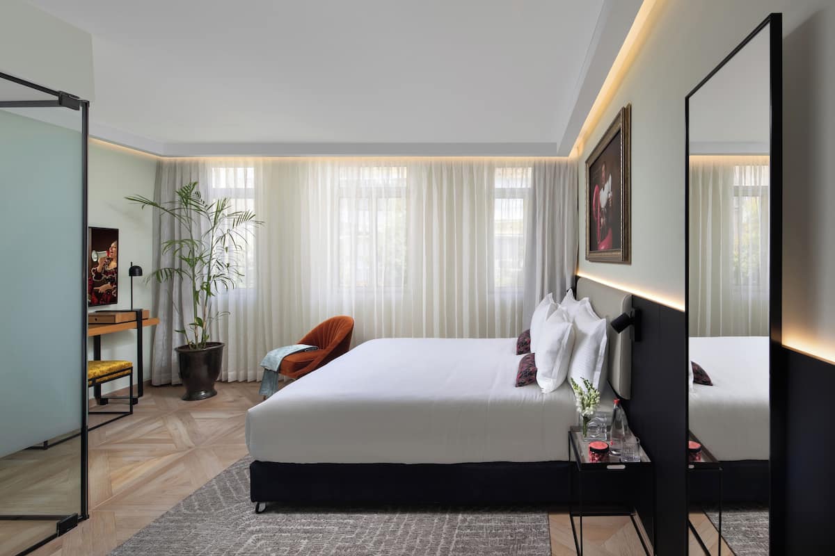 Une chambre d’hôtel moderne avec un grand lit, un bureau avec une chaise, une plante en pot et un miroir.