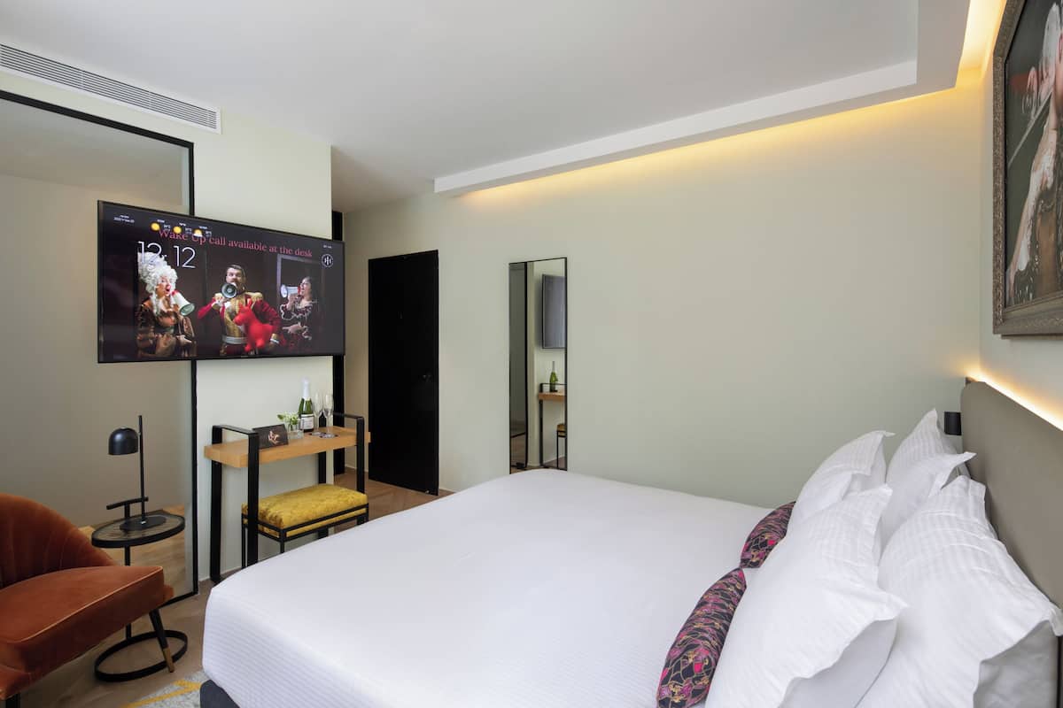 Une chambre d’hôtel avec un lit, un téléviseur fixé au mur, un petit bureau avec une chaise et un miroir.
