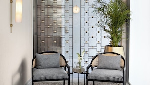 A modern room with two black wicker chairs, a patterned rug, a potted plant, and a decorative wall panel. - Rephael House Boutique Hotel (Rishon LeTsiyon)