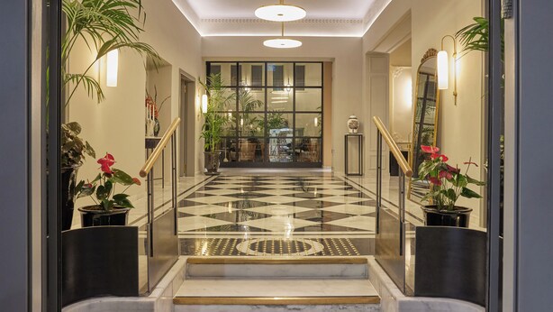 A hotel lobby with a checkered floor, a staircase with golden balusters, and potted plants. - Rephael House Boutique Hotel (Rishon LeTsiyon)