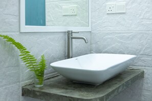Une salle de bain avec un lavabo sur colonne blanc, un robinet moderne et un vase en verre contenant des plantes vertes.