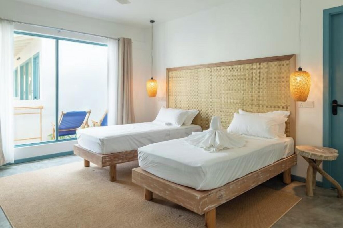 Ein Hotelzimmer mit zwei Betten, einem kleinen Tisch, einem Stuhl und Blick ins Freie.