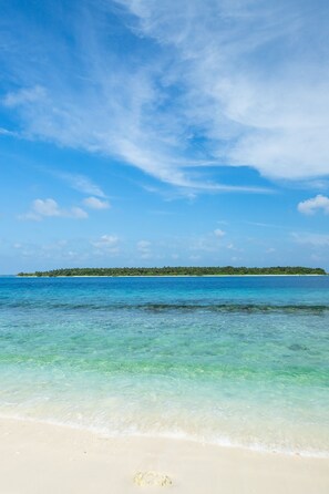 Une plage à l’eau turquoise et limpide, un rivage sablonneux et, au loin, une petite île verdoyante.