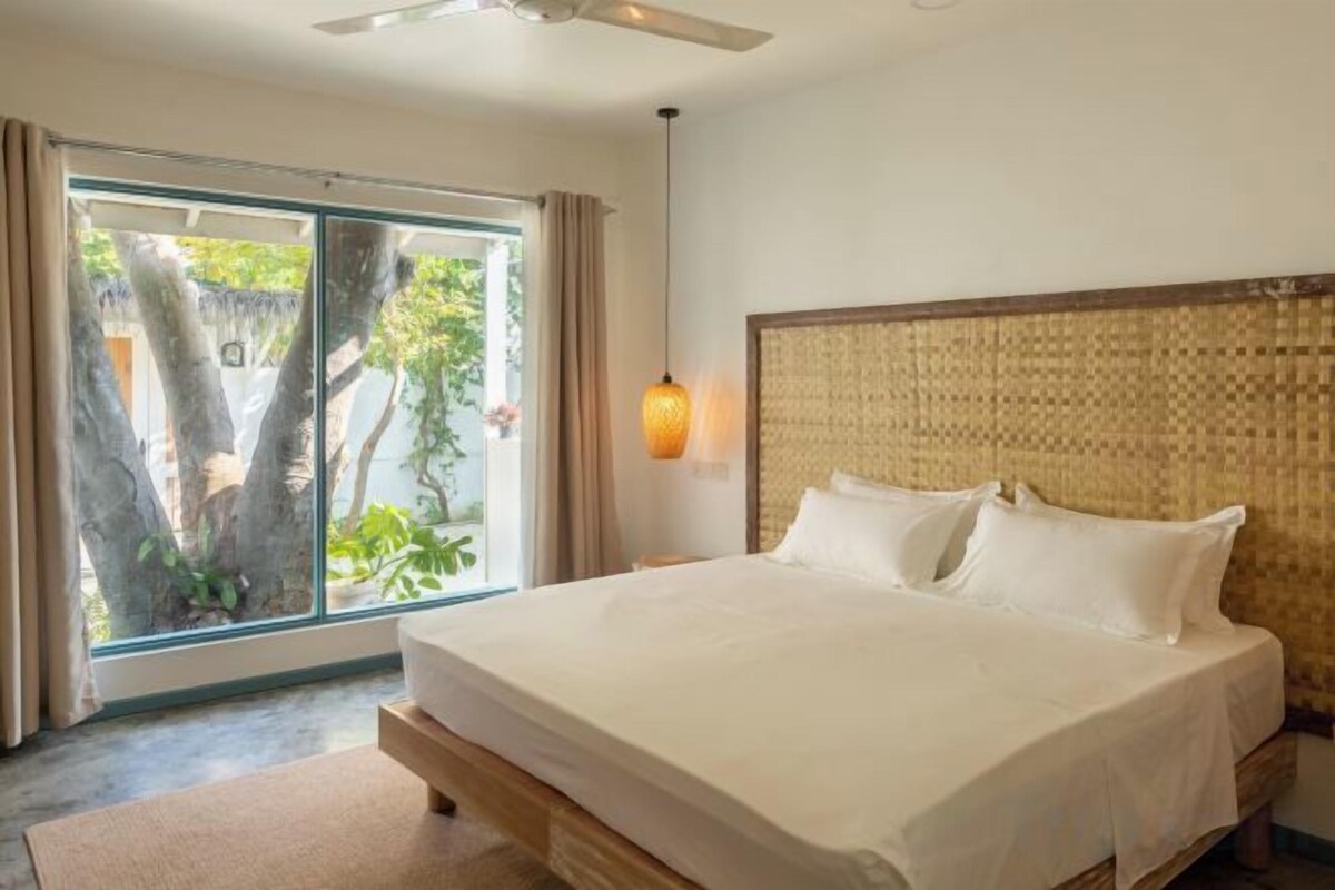 Une chambre d’hôtel avec un lit, un ventilateur de plafond, une fenêtre avec des rideaux et un luminaire fixé au mur.