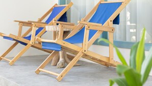Two wooden beach chairs with blue cushions on a balcony with large windows and a white wall. - Manta Reserve (Maalhos)