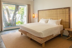 Une chambre avec un grand lit, une tête de lit en bois et une vue sur les arbres, visible à travers une porte-fenêtre coulissante.