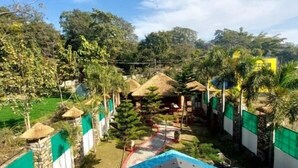 A pool area with a clear view of the surrounding landscape, including trees and a thatched-roof structure. - The Corbett Jungle  (Ramnagar)